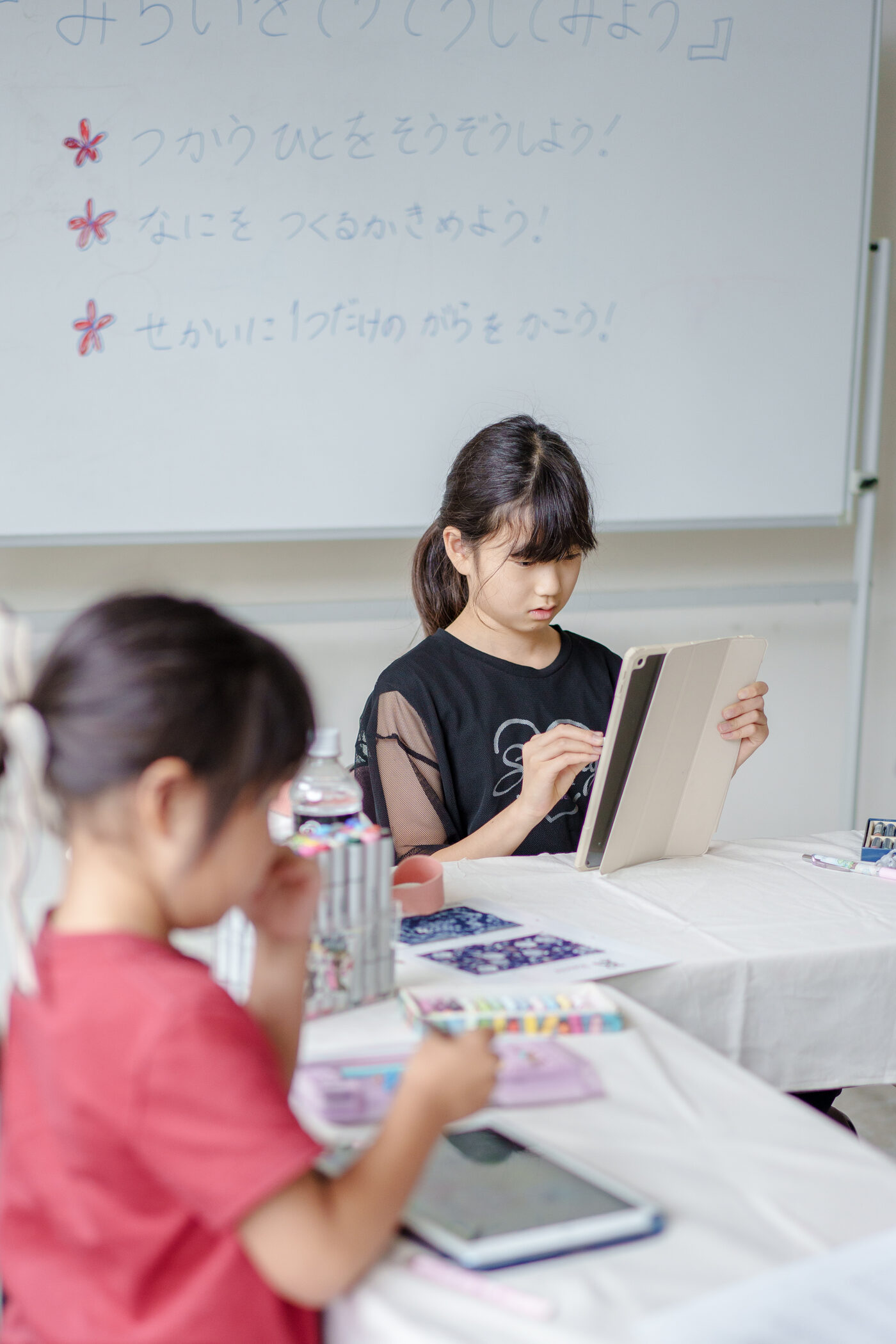 デザインシートに向かう子どもたちと、ホワイトボードに書かれた3つの問い