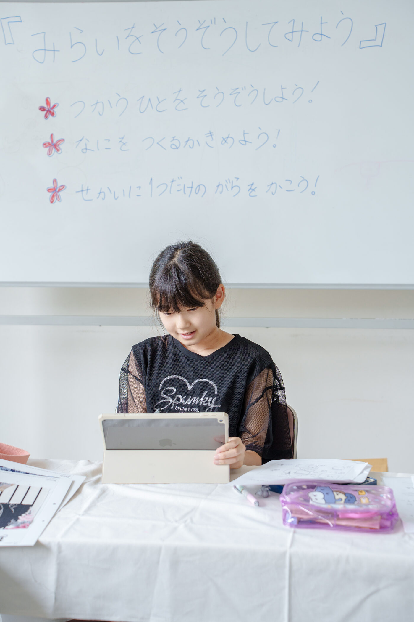 ホワイトボードに書かれた3つの問いと、デザインシートに向かう子ども